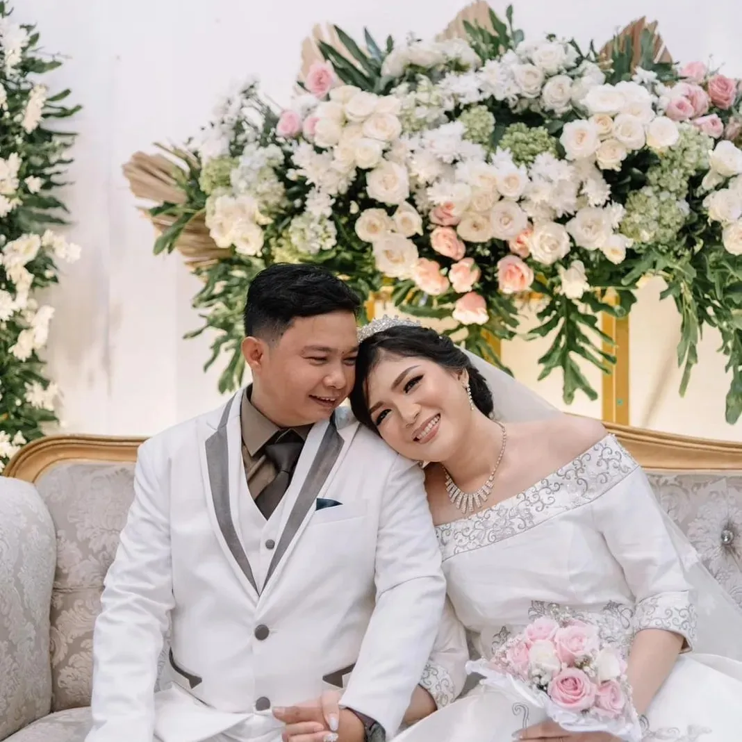 Pasangan pengantin bersandar di depan rangkaian bunga