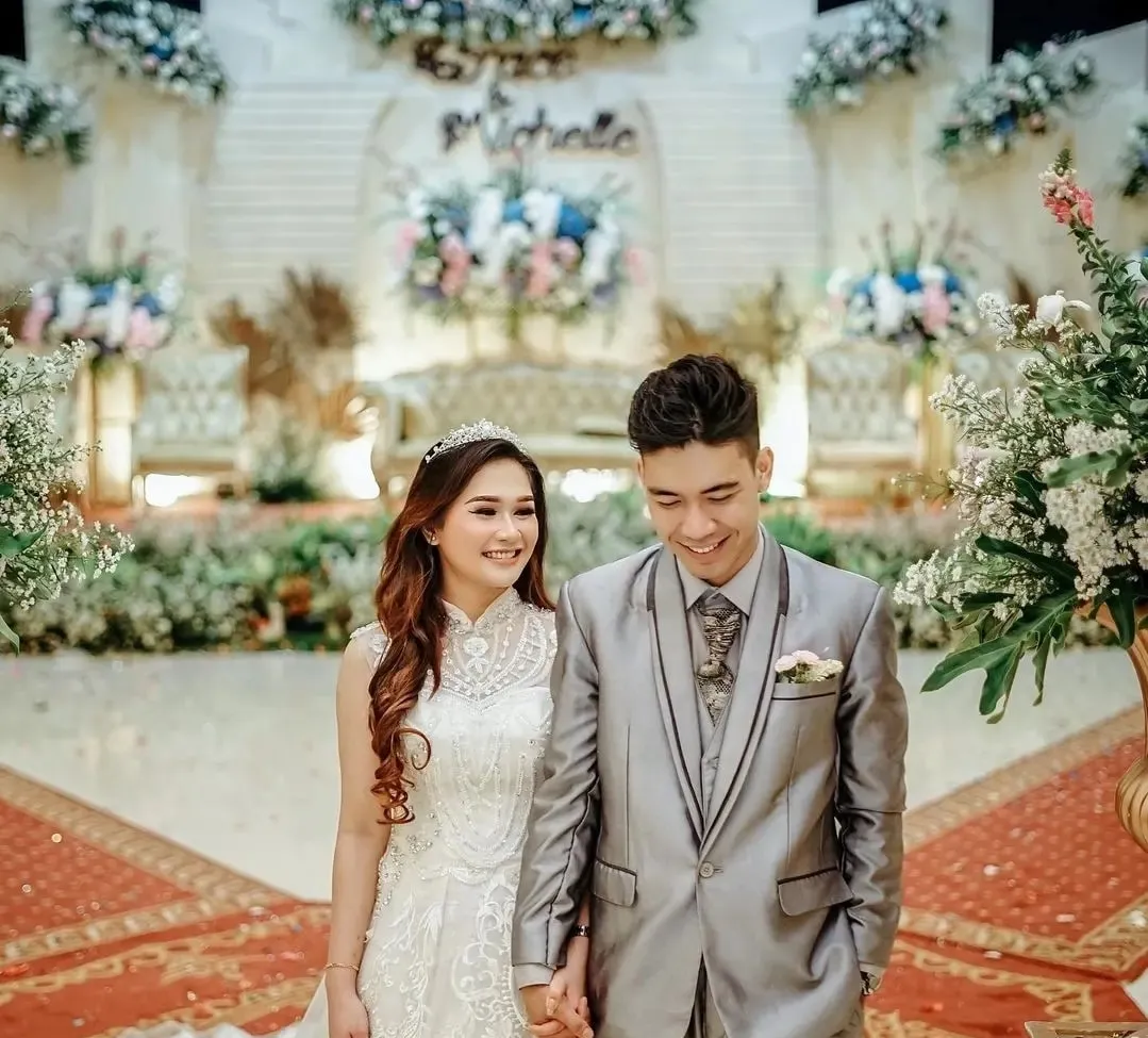 Pasangan pengantin di depan pelaminan bunga