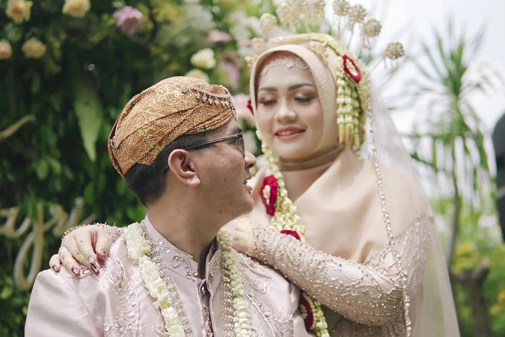 Pasangan pengantin tertawa bersama di depan rangkaian bunga