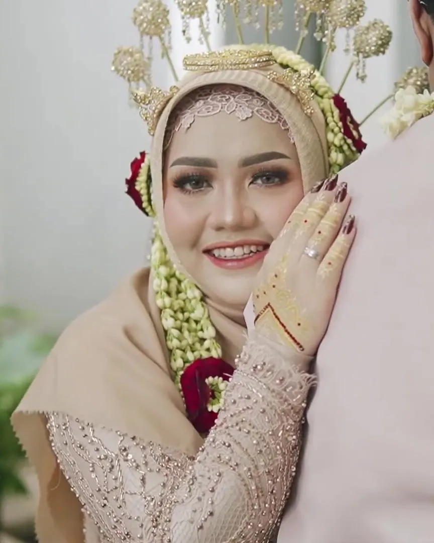 Pengantin wanita berhijab tersenyum sambil bersandar di bahu pengantin pria